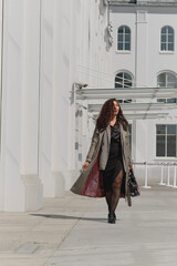 Lady in a trench coat strolling beside a contemporary white building, basking in sunlight. Concept: Reflecting the harmony between personal fashion choices and urban architectural aesthetics