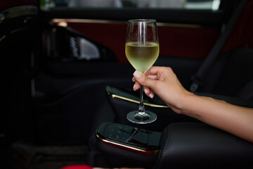 An Elegant Hand Holding a Glass of Exquisite White Wine While in a Luxurious Car Setting
