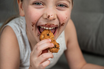 A cute little girl smeared in chocolate eats cookies while lying on the sofa.