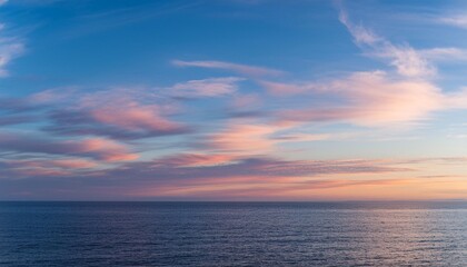 Fototapeta premium Cirrus clouds tinted pink by the sun at sunset over a calm blue ocean