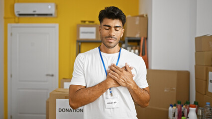 A young hispanic man with a beard is compassionately volunteering at a donation center, displaying positivity.