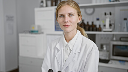 A young, attractive woman in a white lab coat stands confidently in a clinical laboratory setting, radiating professionalism