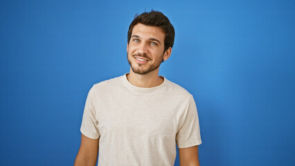 Handsome young hispanic man with a beard standing against a blue background outdoors