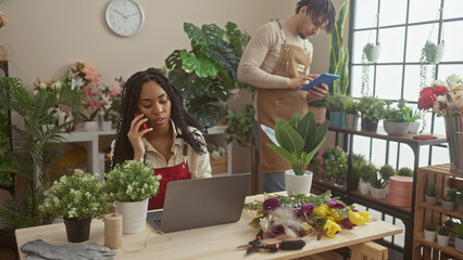 A woman and man work together in a vibrant flower shop, surrounded by assorted plants and flowers,...