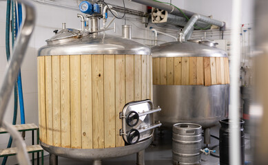 Cylindrical steel fermenters with wood trim and kegs in brewery shop. Craft brewing system. Beer production industry..
