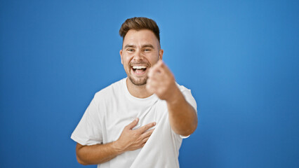 Laughing young hispanic man with a beard pointing joyfully isolated against a blue outdoor wall.