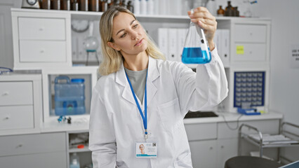 A focused woman scientist examines a blue liquid in flask at an indoor laboratory