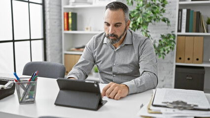 Obraz premium A mature hispanic man with grey beard works attentively in a modern office.