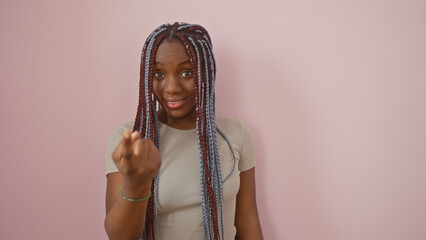 African american woman with braids beckons against a pink isolated background