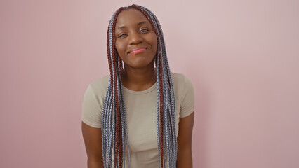 A smiling african american woman with braids against a pink isolated background exudes confidence...
