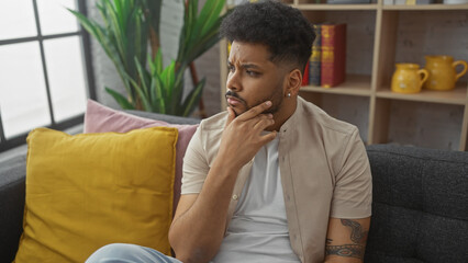 Pensive african american man sitting thoughtfully in a cozy living room interior.