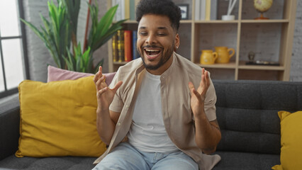 Handsome black man laughing and talking in a well-decorated modern living room, portraying relaxation and happiness.