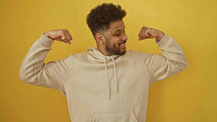 Confident african man flexing muscles against a yellow background, portraying strength and...