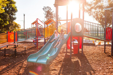 Park playground in afternoon light with children playing on slide