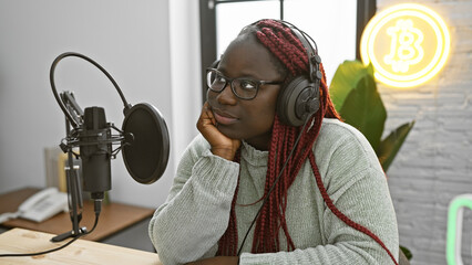 Thoughtful african american woman with braids at a radio studio wearing headphones near a microphone.