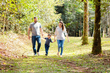 Brazilian family enjoying a sunny walk in nature. Parents hold hands with their cheerful child,...
