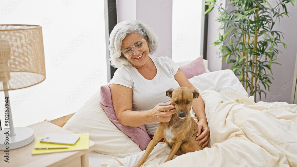 Sticker smiling woman with grey hair petting a brown dog on a bed in a cozy bedroom setting, illuminated by 