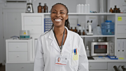 A smiling african american woman clinician with a badge stands confidently in a well-equipped laboratory room.