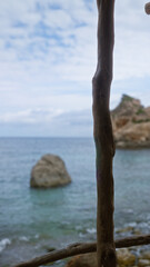Wooden railing framing the serene coast of cala deia in mallorca with rocky outcrops under a partly cloudy sky