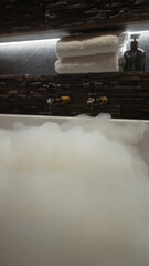 Overflowing bathtub under lit mirror shelf with towels and soap bottle in a bathroom setting