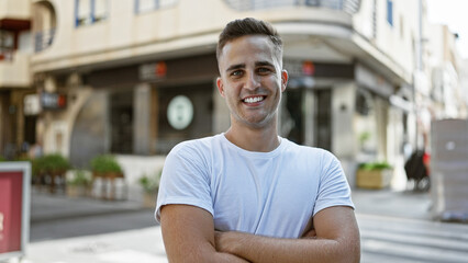 Smiling young hispanic man standing confidently outdoor on a city street