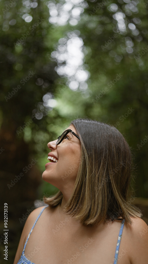 Poster Beautiful hispanic woman with glasses, smiling confidently as she stands amongst kyoto's lush bamboo forest, looking around, full of joy and amazement.