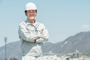 ヘルメットを被った作業着姿の腕組みするアジア人男性作業員
