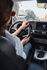 Fototapeta premium Woman driving car focuses on infotainment screen, hands on steering wheel