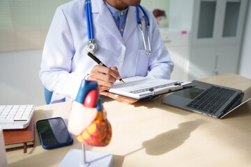 A medical doctor is working at a desk, analyzing patient data related to heart attacks and calculating medical costs to ensure accurate billing and financial management in the healthcare setting.