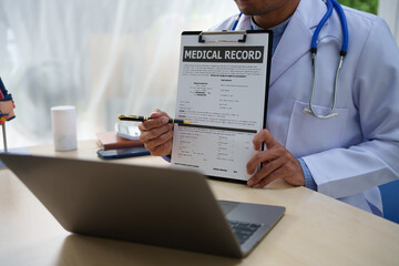 A medical doctor is working at a desk, analyzing patient data related to heart attacks and calculating medical costs to ensure accurate billing and financial management in the healthcare setting.