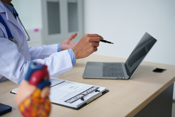 A medical doctor is working at a desk, analyzing patient data related to heart attacks and calculating medical costs to ensure accurate billing and financial management in the healthcare setting.