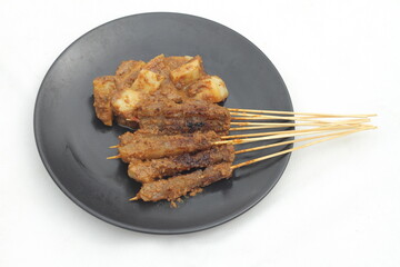 A plate of kikil satay with peanut sauce and pieces of lontong.
