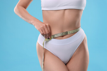 Diet and weight loss concept. Woman with measuring tape showing her slim body against light blue background, closeup