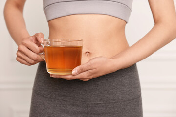 Weight loss concept. Woman with cup of diet tea near white wall, closeup