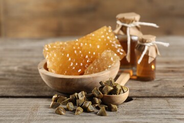 Natural honey tincture, propolis granules and sweet honeycombs on wooden table, closeup