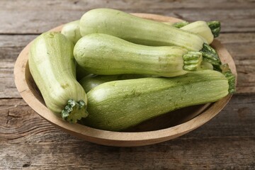 Raw green zucchinis in bowl on wooden table