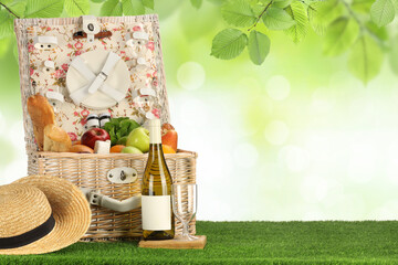 Picnic basket with foods and wine on green grass outdoors. Space for text