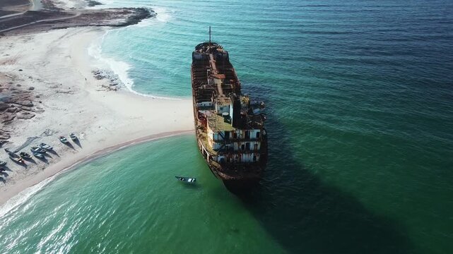 Aerial view of a shipwreck on the rugged coast of Socotra Island, with turquoise waters contrasting against the rusting vessel and rocky shoreline.