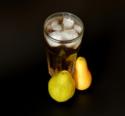 A mixture of pear juices of different varieties in a tall faceted glass with ice on a black background, next to ripe fruit.