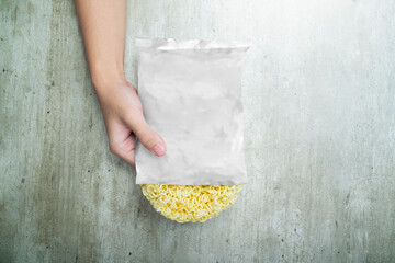 A hand holding a bag of instant noodles with a white plastic bag over it