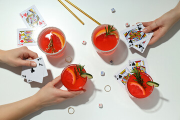 Grapefruit cocktails, cards in hands and rings on white background, top view