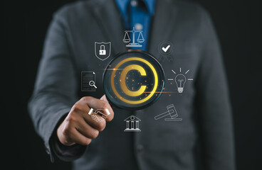 Digital copyright or patent concept. Author rights and patented intellectual property. Businessman holding a magnifying glass focuses on a copyright symbol surrounded by legal icons. trademark license