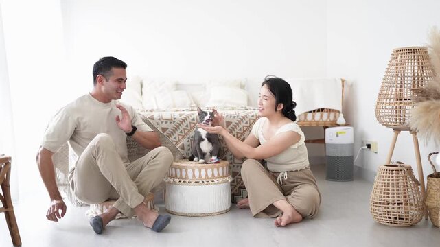 20-something Chinese Malaysian woman and 30-something Malaysian man feeding black and white cats on floor in front of bed in room with Western-style furniture in house in Selangor, Malaysia.