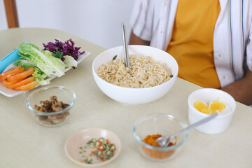 An Instant Noodle In The Bowl With Additional Food On The Table