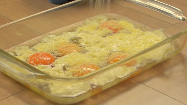 adding parmesan cheese to several eggs with yolks on a glass baking dish. Casserole stewpan protein recipe