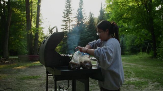 A lady grills kalbi beef in the front yard, backlit by the sun, capturing the rich textures of the meat and the warm glow of sunlight, creating a visually appealing outdoor cooking scene.