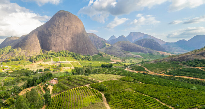 Aerial view of rural landscape of Aguia Branca, ES, Brazil, highlighting conilon coffee plantations set against the backdrop of rocky mountains.