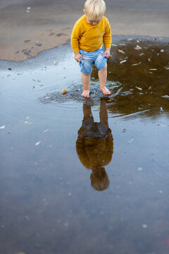 little blonde kid splashing in a puddle with reflection after rain