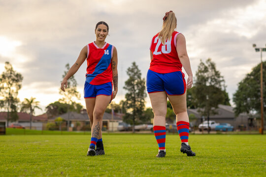 two young women in red and blue team colours on football field going in opposite directions
