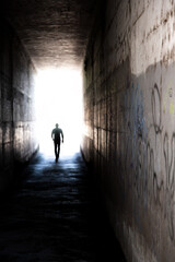 Mysterious tunnel with human figure walking toward the light.